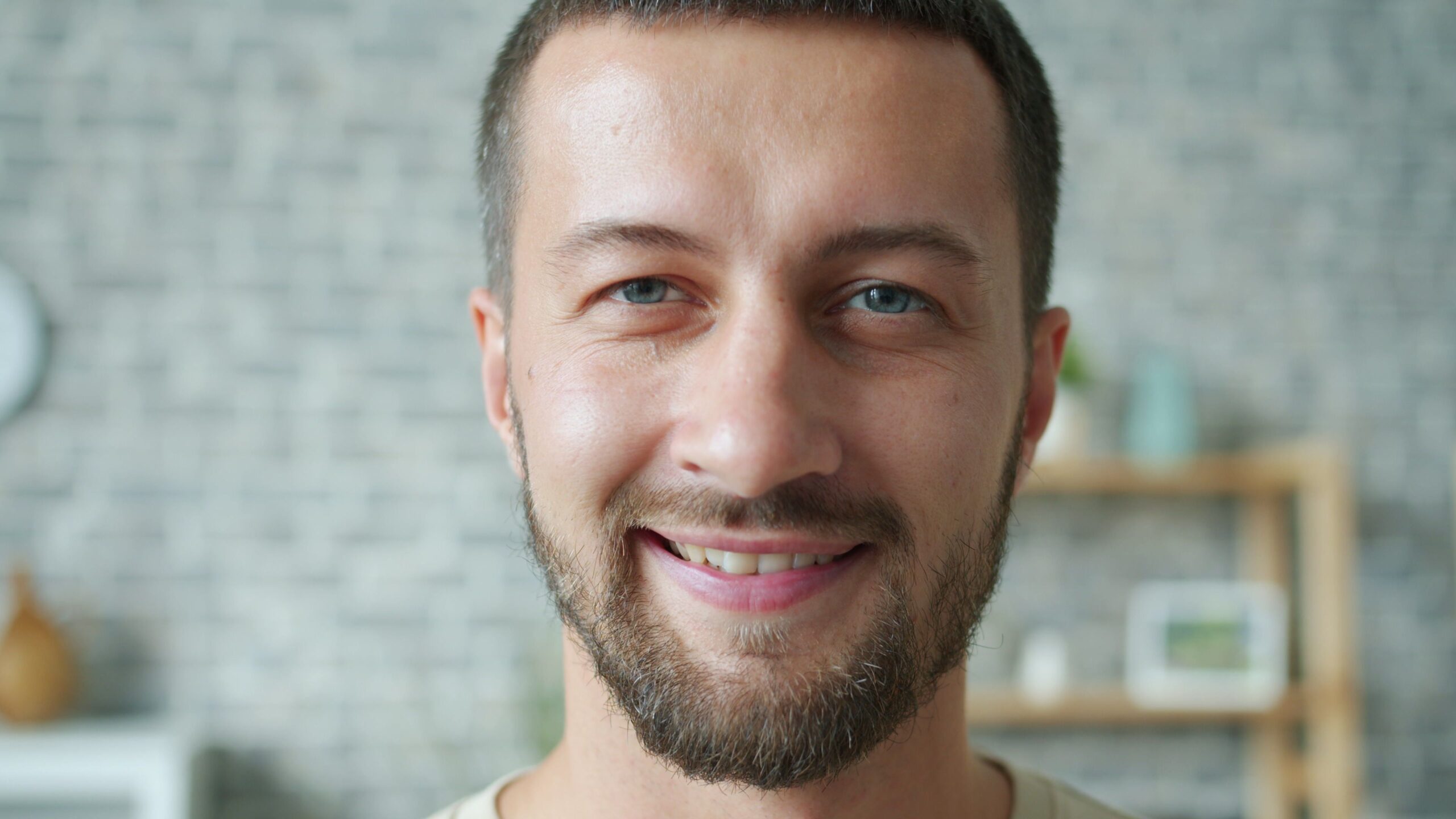 Home Portrait of a smiling man indoors with a blurred brick wall in the background.