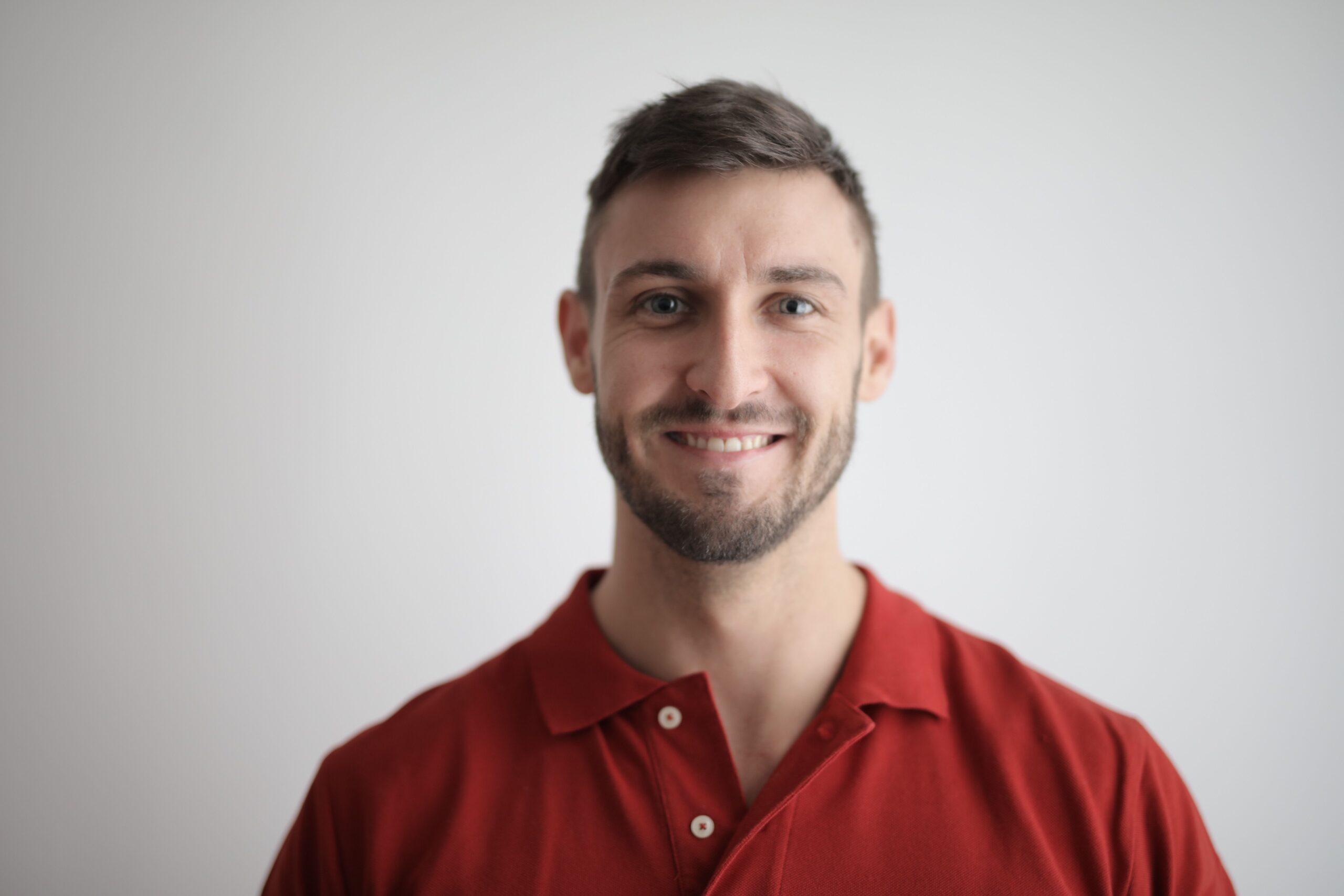 Home Headshot of a happy man with a beard wearing a red polo shirt against a white background.